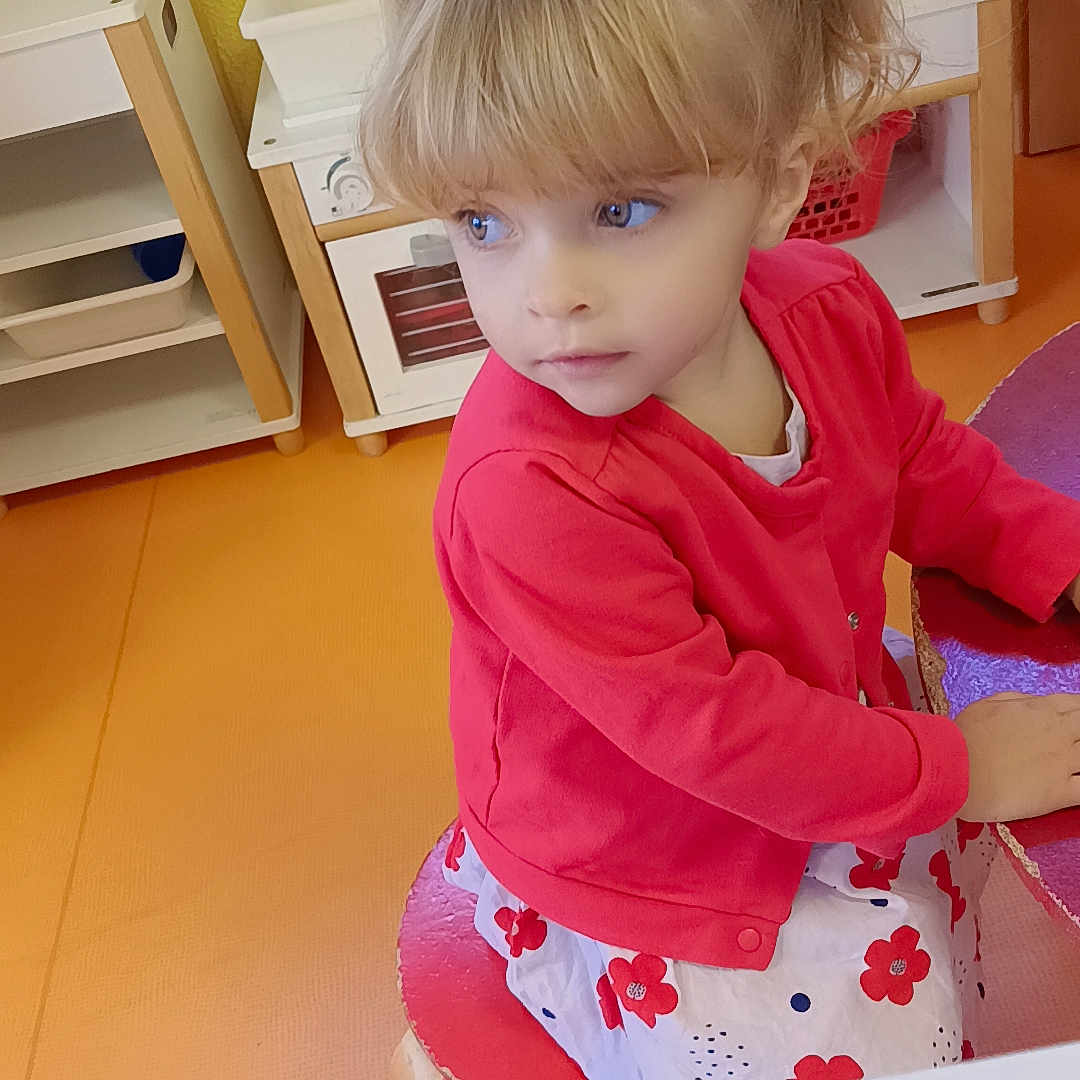 Mia a rejoint le concours — aidez-le/la à gagner de superbes lots ! blonde_hair, blue_eyes, chair, child, childhood, cute, flower_dress, furniture, girl, indoor, kid, orange_floor, pigtails, playroom, portrait, red_cardigan, sitting, table, thoughtful, yellow_wall