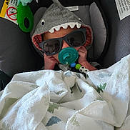 Jesse joined the competition — help win amazing prizes! baby, car_seat, pacifier, sunglasses, hoodie, shark_costume, blanket, plush_toy, infant, child, cute, sleeping, comfort, indoors, accessory, face, headwear, toy, rest, cozy