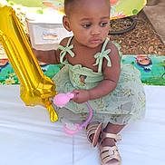 Na'Ryhia Smith joined the competition — help win amazing prizes! toddler, child, balloon, green_dress, table, toy, outdoor, party, birthday, decorations, cartoon_backdrop, sandals, curly_hair, cute, festive, celebration, young_child, sitting, holding, event