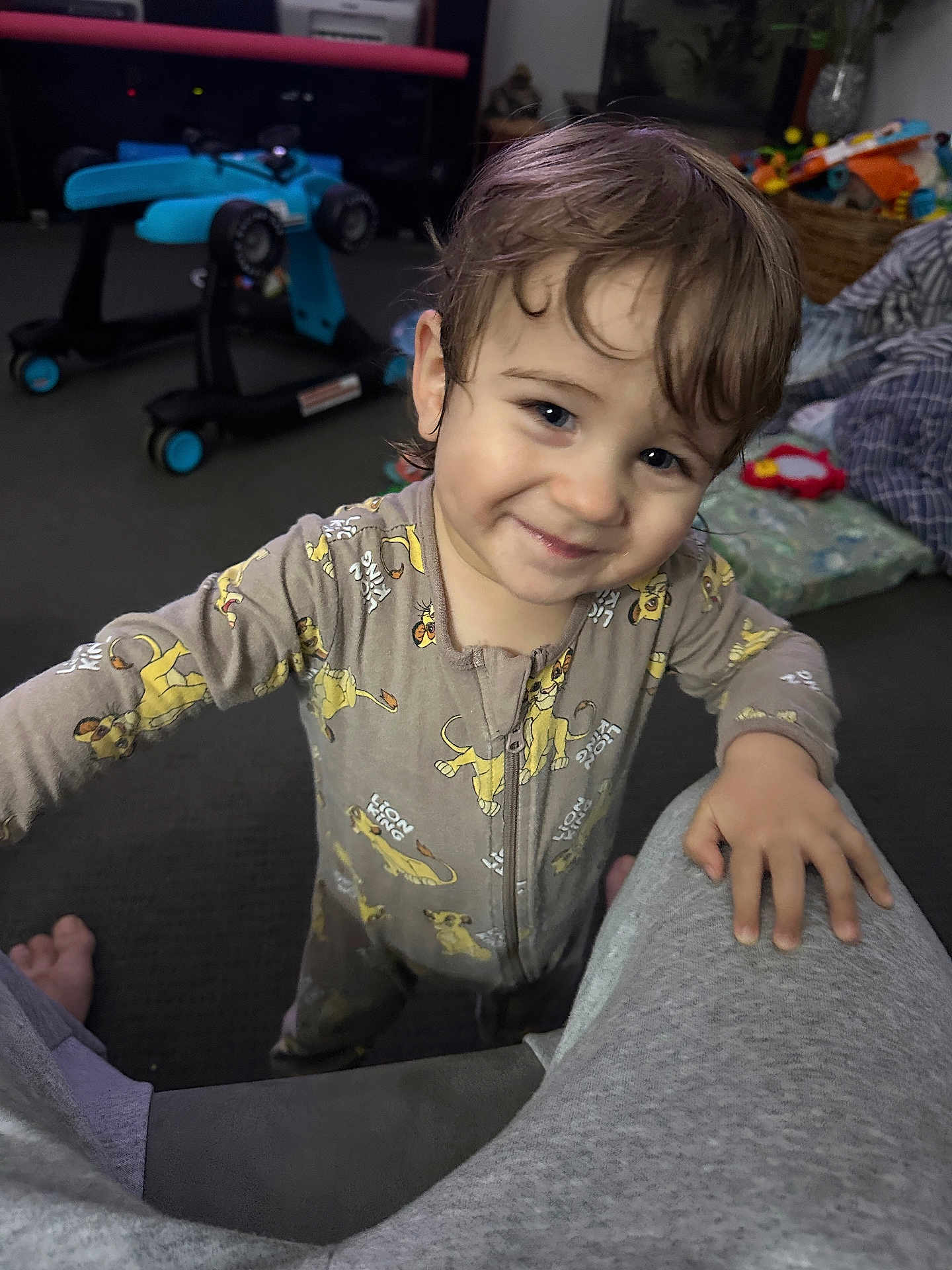 Liam joined the competition — help win amazing prizes! toddler, child, smile, pajamas, lion_king, indoor, carpet, toy, walker, person, face, hand, hair, living_room, basket, blanket, foot, clothing, expression, home