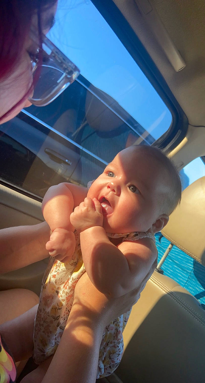 Evalynn is registered to the contest to win money with this photo: auto_part, automotive_exterior, baby, car_seat, chest, comfort, event, finger, fun, gesture, happy, leisure, mouth, nail, person, skin, sky, smile, thumb, toddler