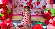 Elena is registered to the contest to win money with this photo: child, birthday_party, balloons, cake, strawberry, pink, red, green, dress, smiling, table, party_decorations, gift_bags, celebration, young_girl, happy, food, indoor, party, festive