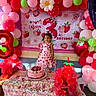 child, birthday_party, balloons, cake, strawberry, pink, red, green, dress, smiling, table, party_decorations, gift_bags, celebration, young_girl, happy, food, indoor, party, festive