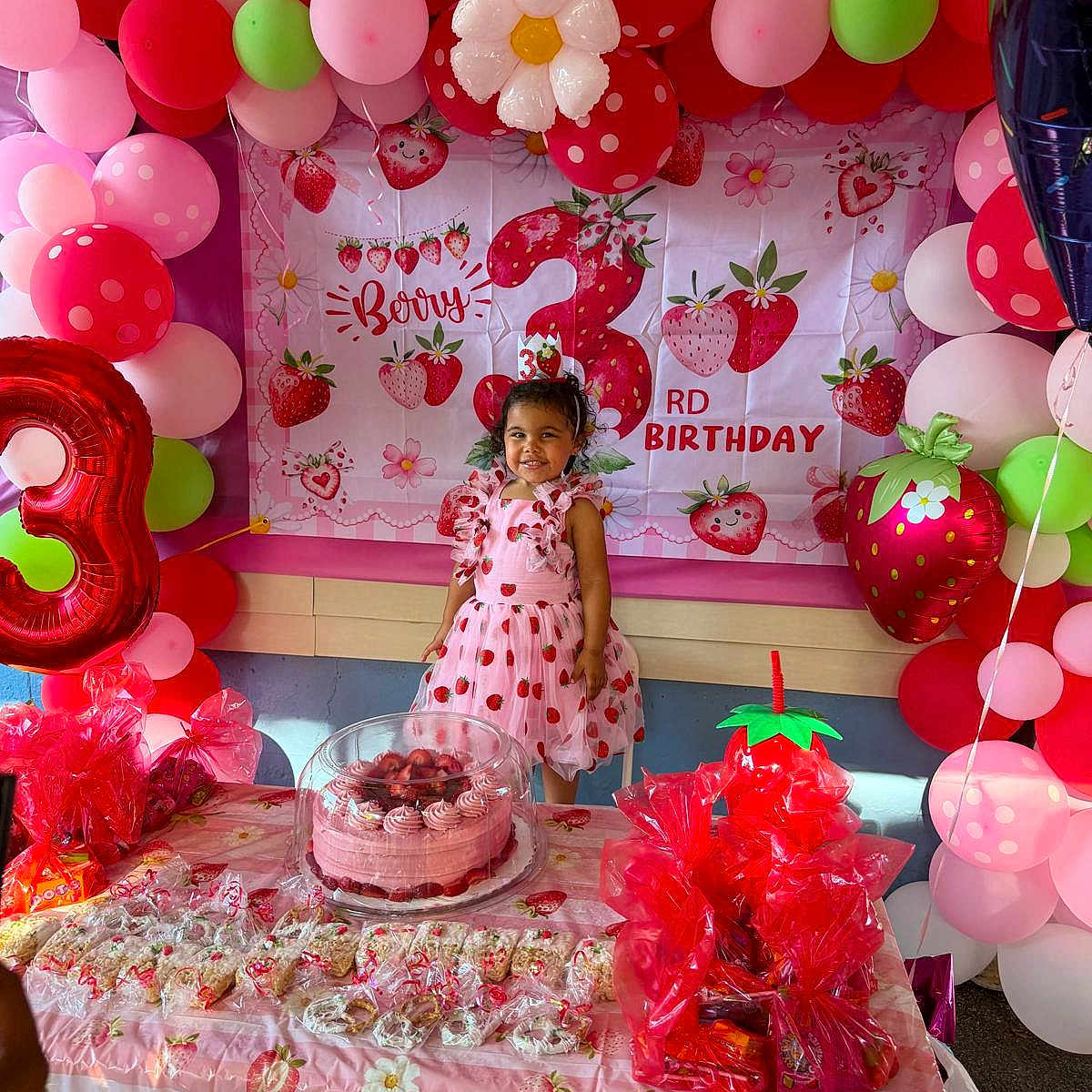 Elena is registered to the contest to win money with this photo: child, birthday_party, balloons, cake, strawberry, pink, red, green, dress, smiling, table, party_decorations, gift_bags, celebration, young_girl, happy, food, indoor, party, festive