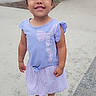 child, girl, purple_dress, sandal, outdoor, sidewalk, heart_doodle, smiling, standing, daylight, casual_clothing, happy, young_child, people_in_background, urban, nature, trees, pavement, summer, cute