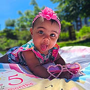 Emiely joined the competition — help win amazing prizes! baby, infant, child, pink_flower_headband, tongue_out, heart_shaped_sunglasses, blanket, milestone_card, outdoor, sunny, greenery, playful, cute, colorful_clothing, closeup, portrait, summer, happy, nature, infant_milestone