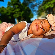 Emiely is registered to the contest to win money with this photo: baby, child, smiling, tutu, headband, bow, outdoor, sunlight, blanket, portrait, happy, cute, infant, nature, greenery, blue_sky, person, lying_down, toddler, soft