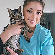 Grace is registered to the contest to win money with this photo: woman, cat, indoor, smiling, pet, animal, human, scrubs, ceiling_fan, holding, portrait, happy, friendly, domestic_cat, tabby_cat, fur, person, young_adult, casual, home
