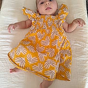 Naëlya participe au concours pour gagner de l'argent avec cette photo : baby, infant, child, dress, yellow, leaf_pattern, lying_down, white_background, soft_texture, barefoot, arm, leg, head, face, expression, indoors, fabric, smiling, cute, person