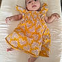 baby, infant, child, dress, yellow, leaf_pattern, lying_down, white_background, soft_texture, barefoot, arm, leg, head, face, expression, indoors, fabric, smiling, cute, person