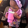 baby, child, girl, headband, pink, sippy_cup, high_chair, clothing, socks, patterned_dress, indoor, seated, curious, cute, toddler, purple, bow, hands, face, table