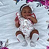 Erynomie is registered to the contest to win money with this photo: baby, infant, child, smiling, lying_down, headband, white_blanket, floral_pattern, pink_flowers, purple_flowers, cute, happy, socks, clothing, person, portrait, hand, fingers, background, indoors