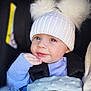 baby, child, face, hat, pom_poms, blue_blanket, sweater, stroller, portrait, cute, infant, warm_clothing, hand, smile, cozy, soft_texture, indoor, close_up, headwear, adorable