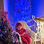 baby, child, christmas_tree, holiday, red_clothing, hat, chair, decorations, lights, reindeer, festive, indoor, winter, cozy, ornaments, white_tree, blue_lights, smiling, cute, seasonal