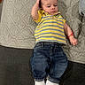 baby, child, infant, striped_shirt, yellow_shirt, jeans, blue_jeans, white_sneakers, bracelet, red_bracelet, blanket, gray_blanket, carpet, indoor, portrait, cute, clothing, laying_down, person, young_child