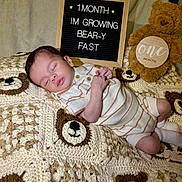 Jvanni is registered to the contest to win money with this photo: baby, infant, sleeping, blanket, crochet, bear, teddy_bear, sign, letter_board, clothing, onesie, cute, soft, cozy, newborn, child, portrait, indoor, rest, adorable