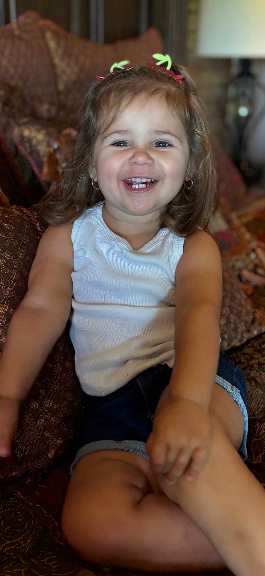 Gracie joined the competition — help win amazing prizes! child, toddler, smiling, happy, sitting, indoor, couch, clothing, tank_top, denim_shorts, hair_clips, cute, portrait, face, person, skin, furniture, home, relaxed, joy