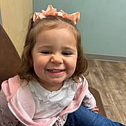 Gracie joined the competition — help win amazing prizes! child, toddler, smiling, girl, pink_bow, hoodie, blue_jeans, indoor, chair, happy, cute, casual_clothing, portrait, seated, brown_chair, wood_floor, light_wall, young_child, playful, small_person