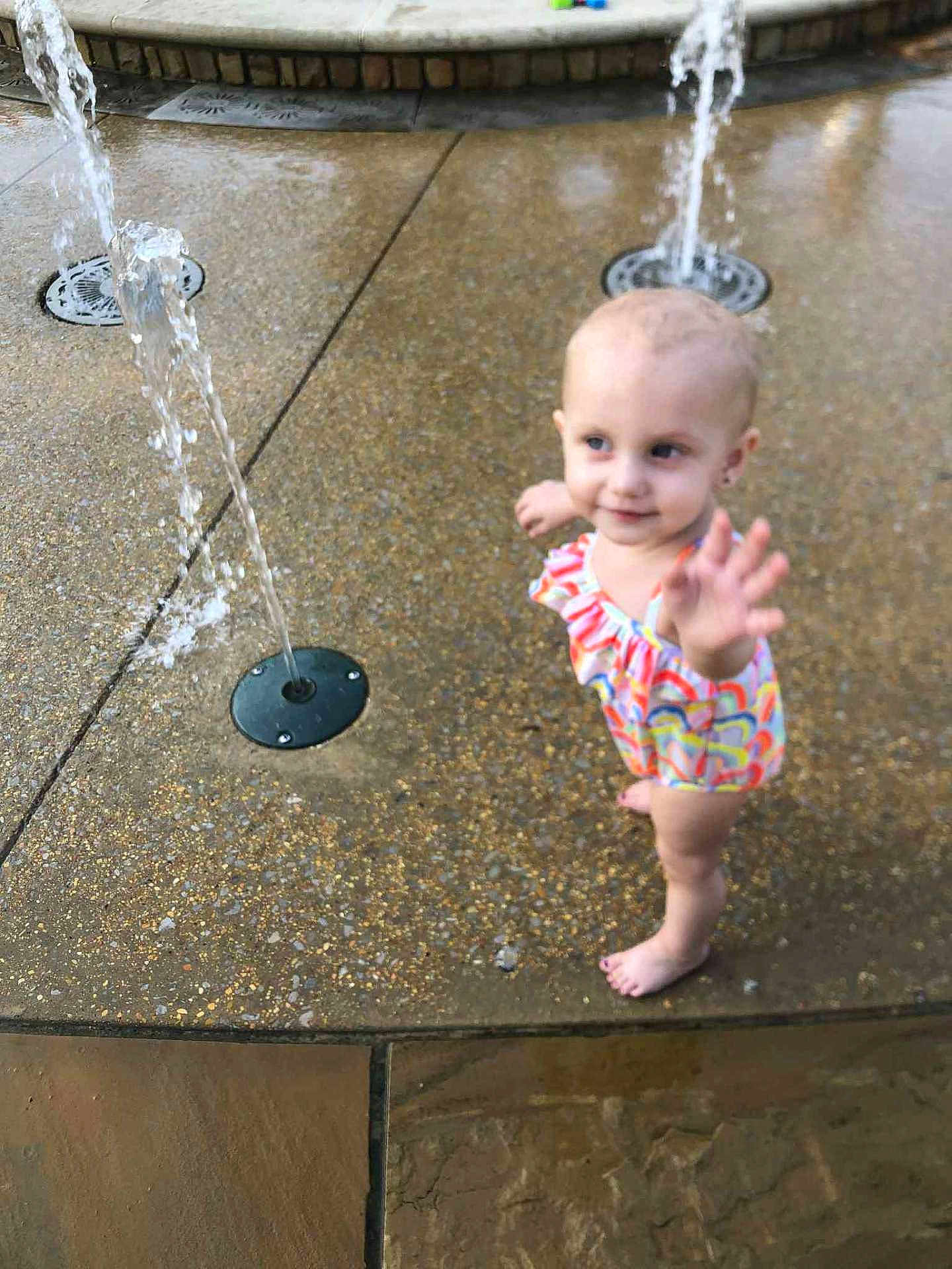 Jalice joined the competition — help win amazing prizes! toddler, child, water_fountain, play, swimsuit, barefoot, outdoor, water, fun, summer, curious, wet_surface, colorful, young_child, reaching, happy, park, fountain, playground, daytime