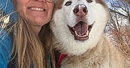 Brady is registered to the contest to win money with this photo: blue_jacket, canine, closeup, daylight, dog, friendship, fur, glasses, happy, husky, nature, outdoor, pet, portrait, sky, smiling, snow, tree, winter, woman