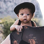 Typhuryn is registered to the contest to win money with this photo: baby, child, black_cap, hand, shoulder, adult, floral_pattern, sheer_clothing, outdoor, nature, mountain, portrait, curious, expression, skin, person, closeup, daylight, young_child, holding