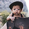 baby, child, black_cap, hand, shoulder, adult, floral_pattern, sheer_clothing, outdoor, nature, mountain, portrait, curious, expression, skin, person, closeup, daylight, young_child, holding