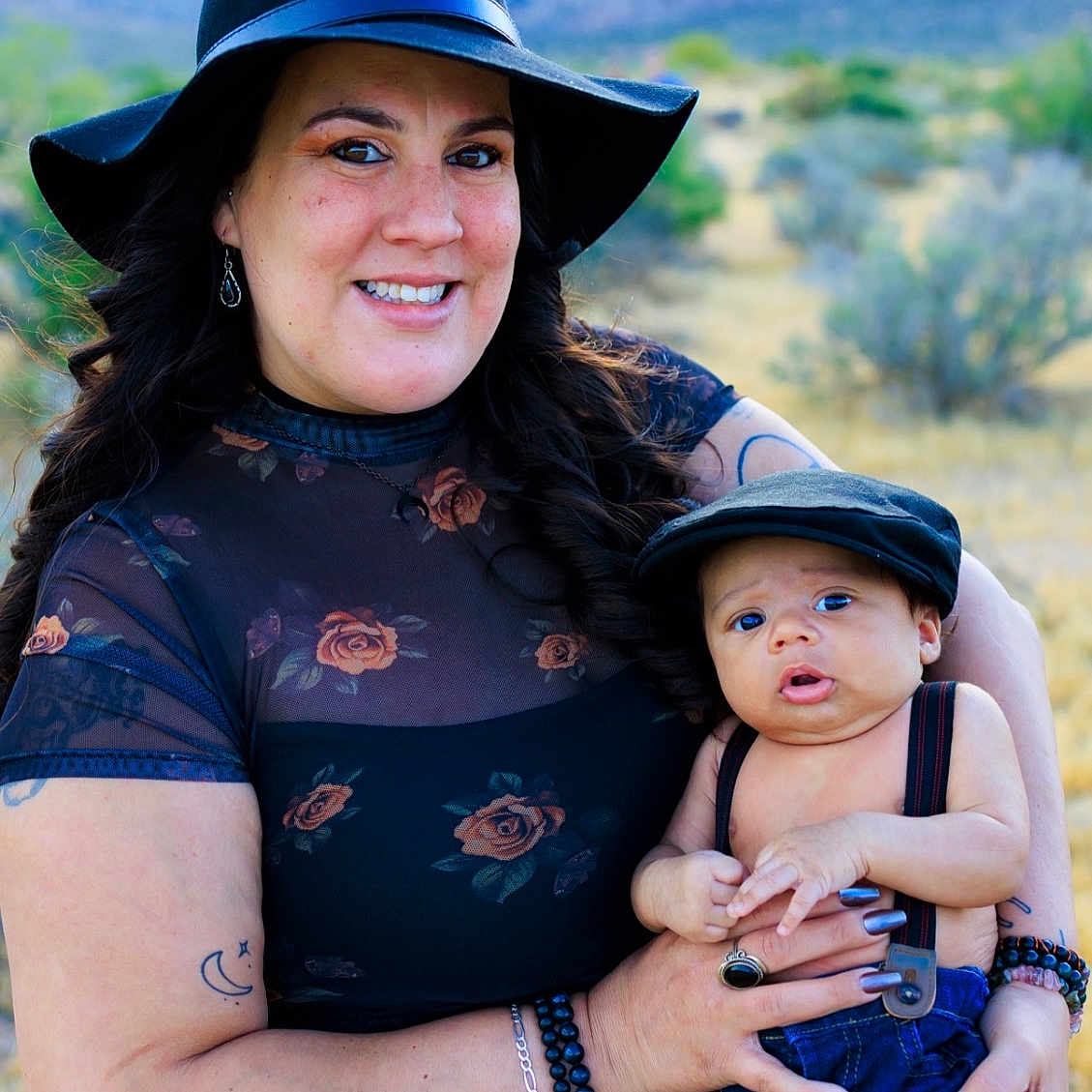 Typhuryn is registered to the contest to win money with this photo: woman, baby, hat, outdoor, mountains, nature, smile, holding, child, portrait, clothing, suspenders, cap, bracelet, tattoo, earrings, grass, trees, scenery, family