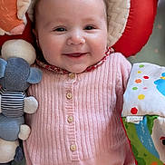 Victoire participe au concours pour gagner de l'argent avec cette photo : baby, infant, smiling, face, cheeks, eyes, onesie, pink_clothing, plush_toy, stuffed_animal, pillow, headrest, blanket, toy_book, buttons, cozy, closeup, portrait, nursery, happy