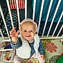 baby, books, child, colorful, cute, floor, furniture, happy, headband, indoor, person, playmat, reaching, safety_bars, seated, smiling, socks, toddler, toys, vest