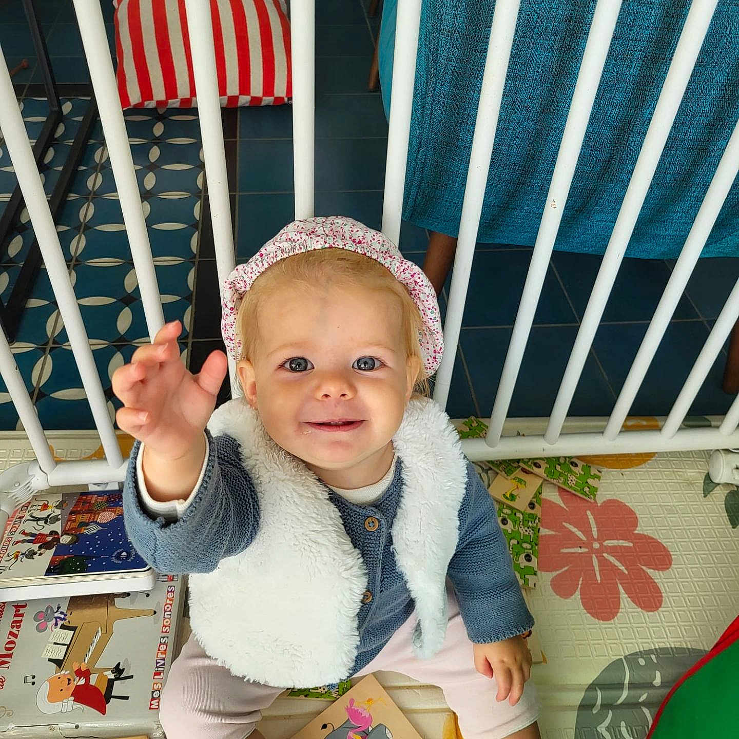 Chjara participe au concours pour gagner de l'argent avec cette photo : baby, books, child, colorful, cute, floor, furniture, happy, headband, indoor, person, playmat, reaching, safety_bars, seated, smiling, socks, toddler, toys, vest
