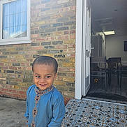 Tayyib is registered to the contest to win money with this photo: ball, blue_outfit, boy, brick_wall, chairs, child, concrete, daylight, door, hand_in_pocket, happy, indoors, outdoor, patterned_tiles, person, smile, tiled_floor, traditional_clothing, window, young