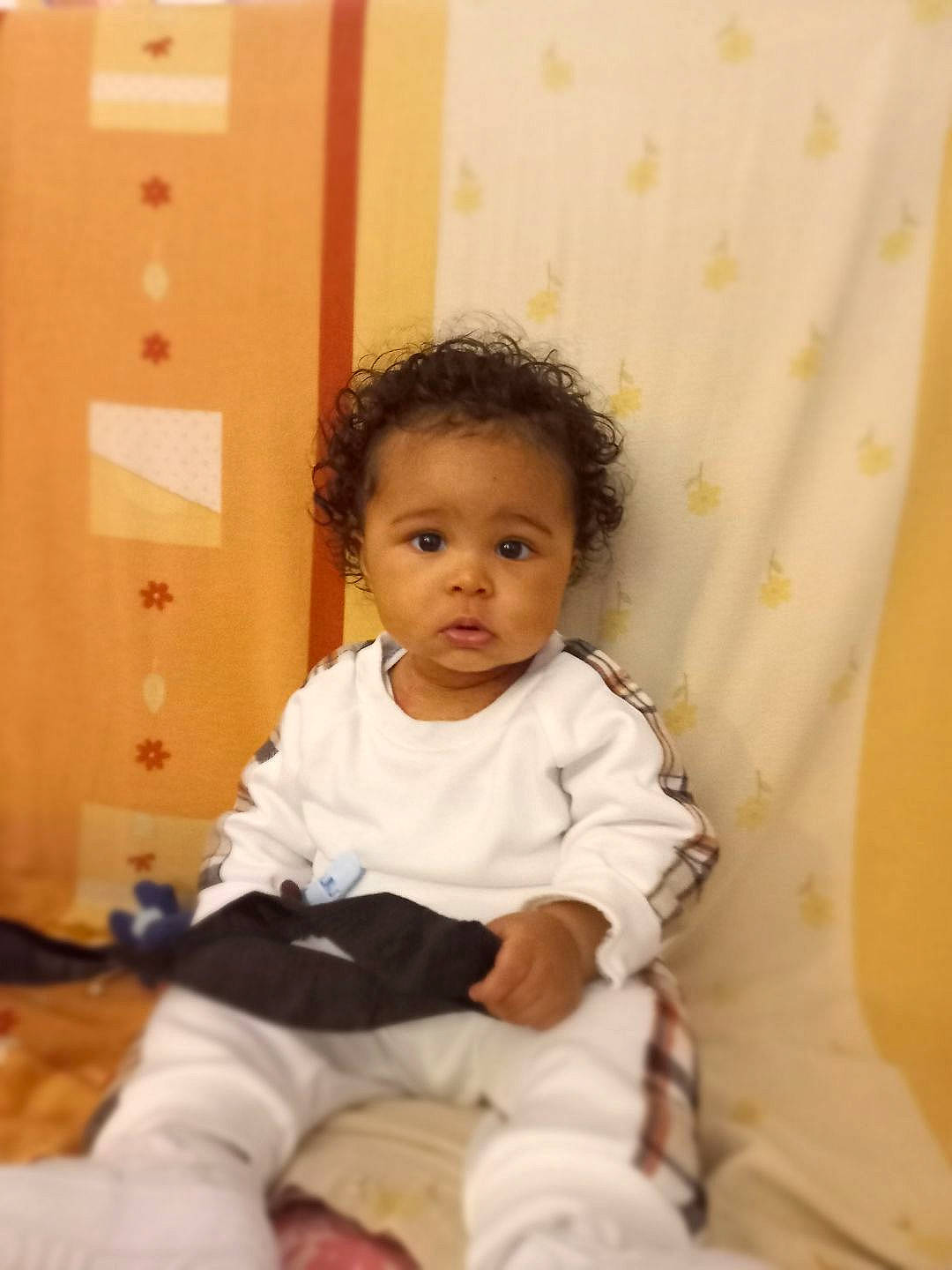 John Junior participe au concours pour gagner de l'argent avec cette photo : baby, baby_toddler_clothing, cheek, child, comfort, curtain, flooring, fun, happy, linens, long_sleeved_t_shirt, person, room, sitting, sleeve, smile, toddler, wood