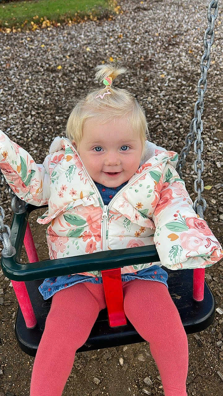 Willow joined the competition — help win amazing prizes! child, toddler, swing, playground, jacket, floral_pattern, pink_tights, blonde_hair, pony_tail, smiling, blue_eyes, outdoor, play, seat, chains, wood_chips, happy, cute, winter_clothing, fun