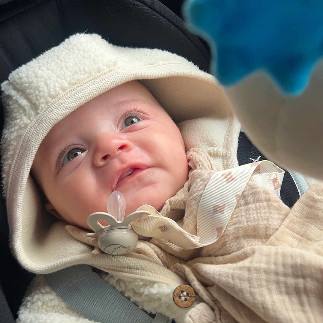 Athyr participe au concours pour gagner de l'argent avec cette photo : baby, blue, car_seat, child, closeup, clothing, curious, cute, expression, face, hood, indoor, infant, jacket, pacifier, portrait, seatbelt, soft, toy, warm