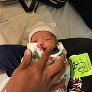 Jonathan is registered to the contest to win money with this photo: newborn, baby, swaddle, hat, hand, bed, blanket, person, infant, cute, sleepwear, resting, indoor, soft, human, clothing, tender, closeup, family, comfort