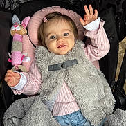 Layla is registered to the contest to win money with this photo: baby, child, clothing, cozy, cute, furry_vest, gray_blanket, happy, indoor, infant, jeans, leopard_print, person, pink_pillow, pink_sweater, plush_toy, portrait, smiling, stroller, waving_hand