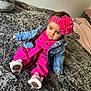 baby, child, denim_jacket, pink_outfit, headband, flower, white_shoes, blanket, bed, fur_texture, cute, indoor, portrait, infant, clothing, sitting, person, fashion, expression, home