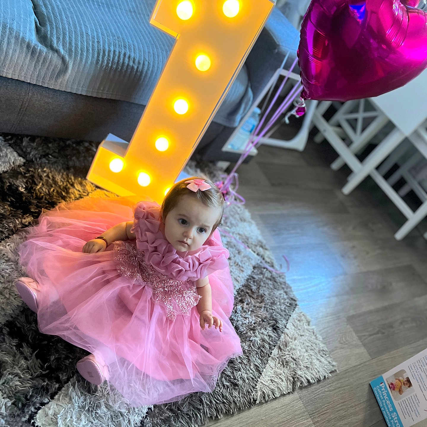 Layla is registered to the contest to win money with this photo: baby, balloons, birthday, celebration, child, couch, decor, flooring, gift_box, girl, heart_shaped, indoor, lighting, number_one, party, pink_dress, portrait, rug, toddler, toy