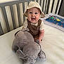 baby, child, smiling, hat, bucket_hat, plush_toy, elephant, crib, nursery, overalls, white_wall, mattress, water_play_mat, happy, sitting, indoor, cute, person, infant, toy