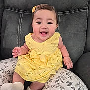 Gianna joined the competition — help win amazing prizes! baby, child, clothing, comfort, couch, cute, fabric, face, hair_clip, happy, indoors, infant, person, pillow, portrait, sitting, smiling, sock, yellow_dress, young_child