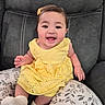 baby, child, clothing, comfort, couch, cute, fabric, face, hair_clip, happy, indoors, infant, person, pillow, portrait, sitting, smiling, sock, yellow_dress, young_child