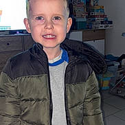 Benji participe au concours pour gagner de l'argent avec cette photo : child, boy, young_boy, smiling, teeth, jacket, puffer_jacket, indoor, living_room, toys, tv_screen, tile_floor, dresser, hair, ears, eyes, pants, flash_photography, portrait, casual_clothing
