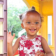 An'Dreya is registered to the contest to win money with this photo: child, girl, toddler, smiling, waving, portrait, face, eyes, teeth, hair_bun, curly_hair, floral_dress, dress, playhouse, window, colorful, yellow, outdoor, daylight, happy