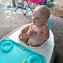Braxtan is registered to the contest to win money with this photo: baby, walker, child, outdoor, concrete_floor, folding_chair, red_chair, plastic, curious, hands_clasped, diaper, seat, person, infant, playtime, daylight, grass, background, pet, container