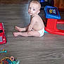 toddler, child, diaper, floor, toy, plastic, play_table, red, blue, curious, indoor, wooden_floor, person, baby, sitting, looking_back, playtime, colorful, home, young_child