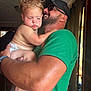 affection, arm, beard, cap, casual_clothing, child, closeup, curtains, diaper, face, family, green_shirt, holding, indoor, man, natural_light, skin, sleepy, toddler, window