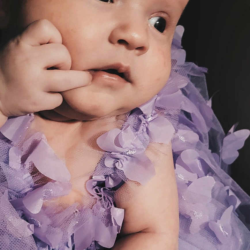 Lottie is registered to the contest to win money with this photo: accessories, baby, bodypart, clothing, dress, face, finger, flower, hand, happy, hat, head, newborn, person, petal, photography, plant, portrait, purple, smile