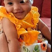 Hazel is registered to the contest to win money with this photo: baby, child, smile, yellow_clothing, headband, sunflower_pattern, arm, couch, indoor, person, happy, portrait, cute, infant, fabric, holding, sitting, skin, bright_colors, furniture