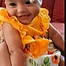 baby, child, smile, yellow_clothing, headband, sunflower_pattern, arm, couch, indoor, person, happy, portrait, cute, infant, fabric, holding, sitting, skin, bright_colors, furniture
