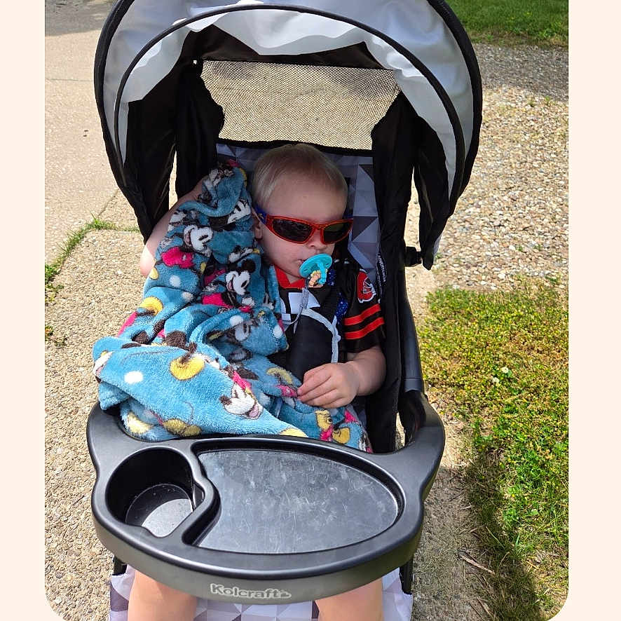 Marcus is registered to the contest to win money with this photo: child, baby, toddler, stroller, sunglasses, red_sunglasses, pacifier, blanket, spiderman, outdoor, sunlight, sidewalk, grass, pavement, portrait, sitting, vehicle, infant, family_photo, screenshot